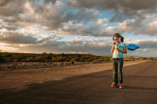 Girl holding balloon standing on desert path with snack