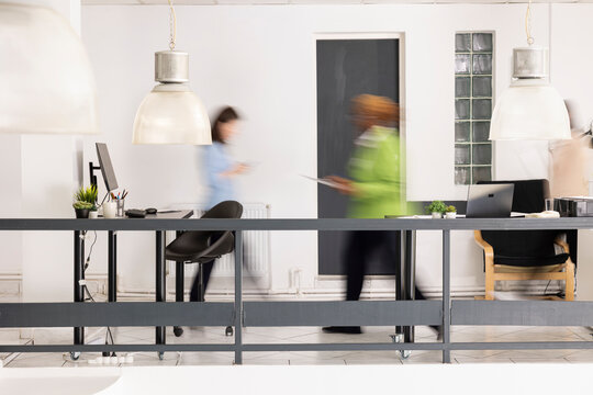 Diverse employees walk through a busy modern office in motion blur, creating a sense of fast paced corporate activity and workplace deadlines.