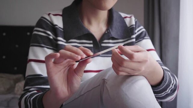 A woman sits by a window filing her nails during a quiet at-home manicure, emphasizing personal grooming, self-care, relaxation and everyday beauty maintenance