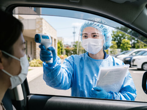 非接触体温計を構えて車内の患者を検温するフェイスシールド姿の女性