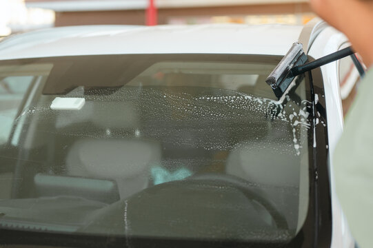 Person cleaning a car windshield with a squeegee during a professional car wash