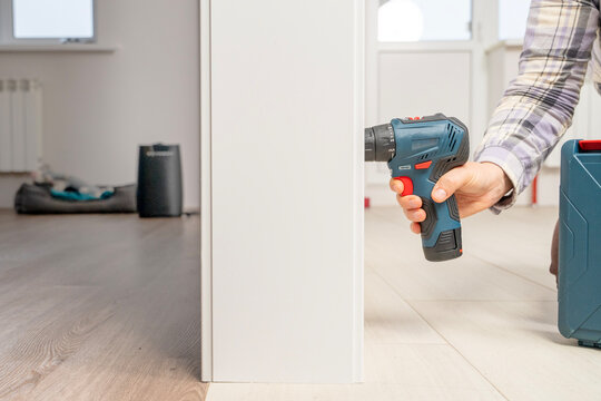 Close view of a persons hand using a cordless drill to assemble furniture inside a bright modern apartment.