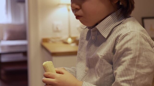 Young child with long brown hair in a striped shirt eating a healthy Canary Island banana as a snack. Concept of healthy eating for kids