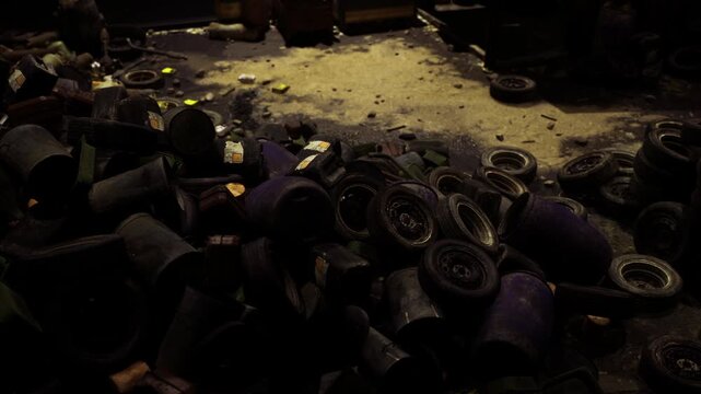 Mountain of tires and scattered drums fading into shadow at predawn, quiet salvage yard mood perfect for reportage about waste industry and urban decay
