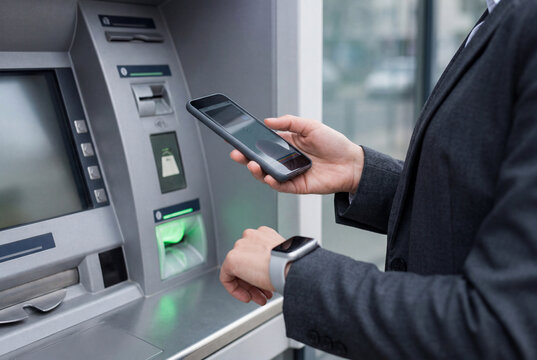 Businesswoman using a smartphone to interact with an automated teller machine for banking