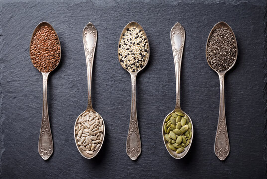 Antique silver spoons filled with assorted healthy seeds on a dark slate