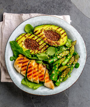Grilled chicken, grilled avocado and asparagus salad with linen seeds. Balanced lunch in bowl. Top view