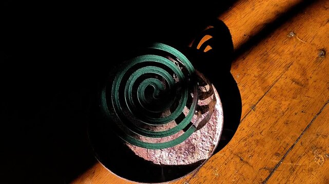 Smoking green mosquito repellent coil burning on a wooden table in soft sunlight