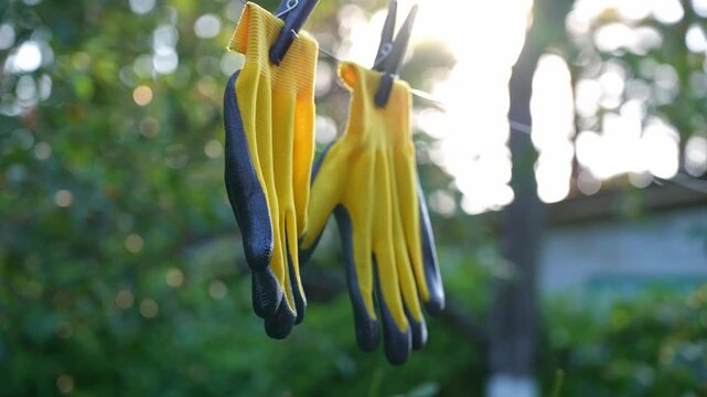 Yellow garden gloves tools dry on rope on greenery outdoor background during sunset. Spring summer gardening season. Concept of hand care hygiene and protection. Housework farm equipment