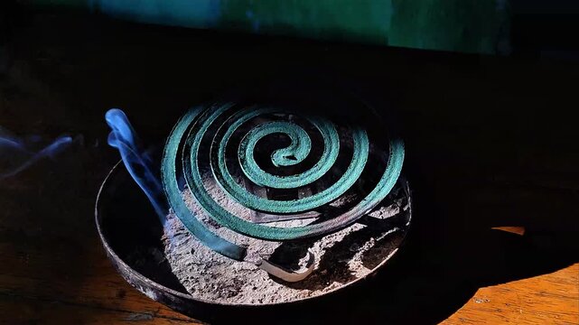 Smoking green mosquito repellent coil burning on a wooden table in soft sunlight