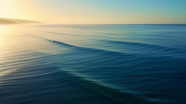 Aerial drone footage of calm ocean waves rolling onto a sandy beach during a golden sunrise