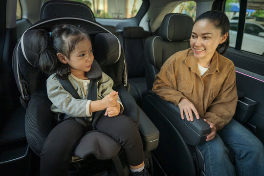 happy mother take care her preschool girl in car seat. play and talking with child