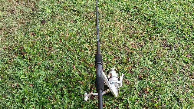 A spinning fishing rod and reel combo placed on a grassy field, featuring a lightweight graphite rod with a silver spinning reel and EVA foam handle grips. Suitable for freshwater and light saltwater 