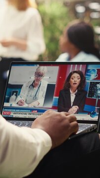 Vertical screen: Black man watching online news segment about artificial intelligence and doctors on laptop during outdoor work break, digital media communication, informal workplace, for AI strategy.