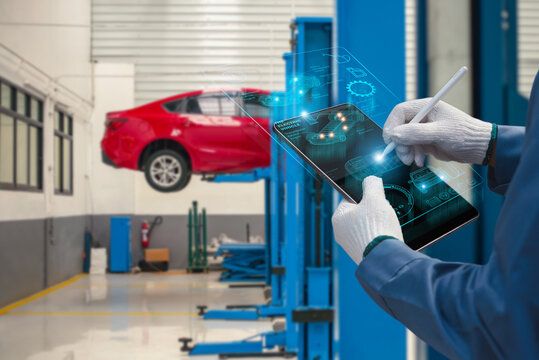Auto mechanic using futuristic holographic tablet for EV car diagnostics in garage, photo manipulation, not AI generated.