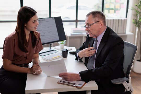 Mature male human resources professional interviewing young asian woman job applicant, discussing employment contract details and career opportunities in a modern office setup