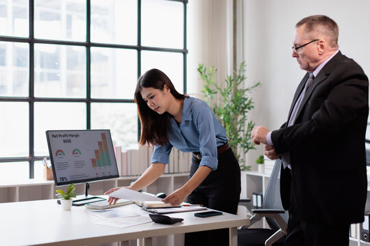 Business people collaborating on financial data analysis, young female employee reviewing documents with an experienced male colleague in a modern office environment
