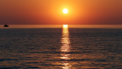 Fototapeta premium Radiant sun sinks below the ocean horizon, casting golden light on waves
