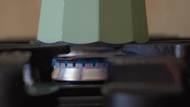 Close up of italian moka pot heating on gas stove with blue flame preparing fresh coffee at home kitchen. 
