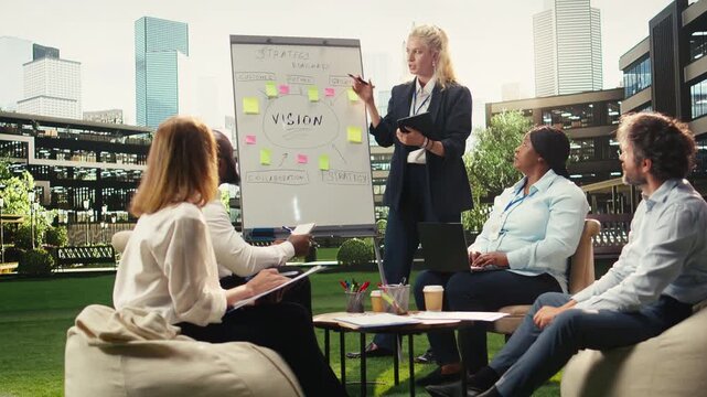Businesswoman pointing at action plan timeline on whiteboard during outdoor workshop, leading colleagues through vision and growth ideas on urban terrace.
