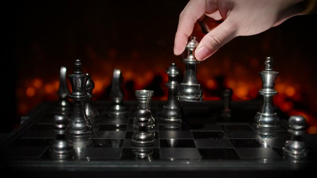 A hand reaching to grab a chess piece on a board with dramatic orange fire-like background lighting in a tense game moment.
