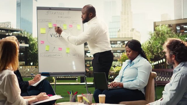 Portrait of diverse businesspeople discussing project timeline on whiteboard during meeting, sharing strategy ideas at outdoor presentation.
