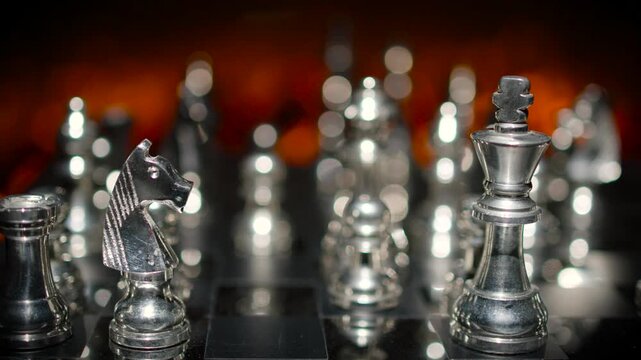 Silver chess pieces arranged on a board with dramatic dark atmospheric lighting and selective focus highlighting key pieces.