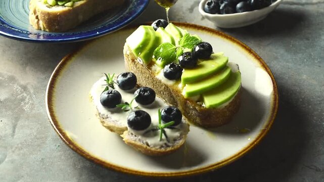 Honey drizzling from a wooden dipper onto fresh avocado and blueberry sourdough toast, served alongside Greek yogurt berry toast on a plate. Delicious, healthy gourmet breakfast concept.