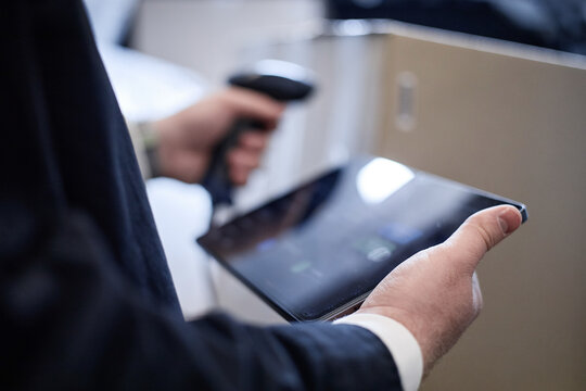 Close up of middle aged businessman scanning package barcode with handheld reader while holding tablet, managing individual storage inventory. Ideal for logistics, warehousing marketing