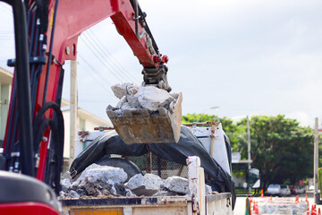 An excavator bucket scooping up broken concrete debris into a dump truck at a road construction site. © Bowonpat