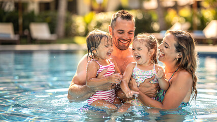 Obraz premium Happy family on summer holiday playing together in swimming pool, parents holding two young daughters safely in water, joyful splashing and laughter, vibrant family bonding moment.