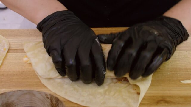 Tortilla rolling. Preparing burrito. Chef cooking shawarma on kitchen table. Gloved hands wrapping flatbread with meat vegetables sauce.