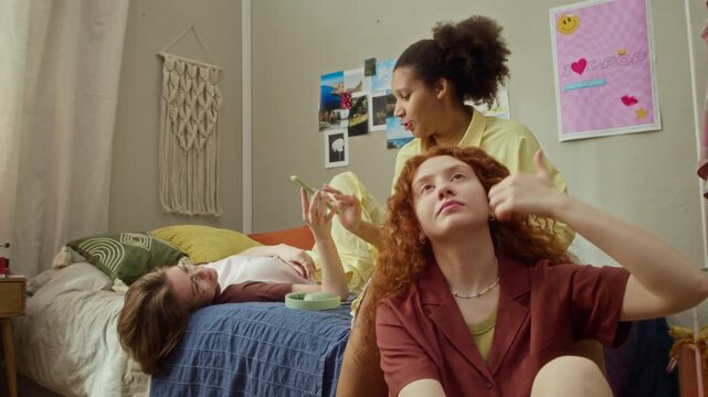 Diverse African American and Caucasian girls relaxing in college dorm room, using smartphone and styling hair. Ideal for youth lifestyle and diversity campaigns