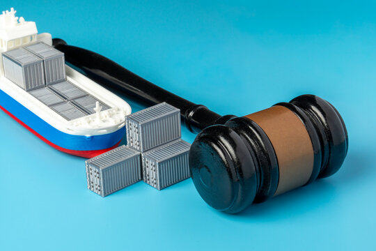 Miniature cargo ship and a judge gavel on a blue background. Maritime law, international trade regulations, customs disputes, shipping embargoes, freight tariffs concept.