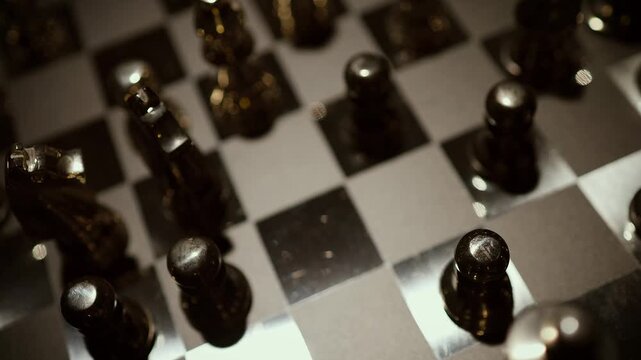 A top-down aerial view of black and silver chess pieces arranged on a classic checkered chess board.