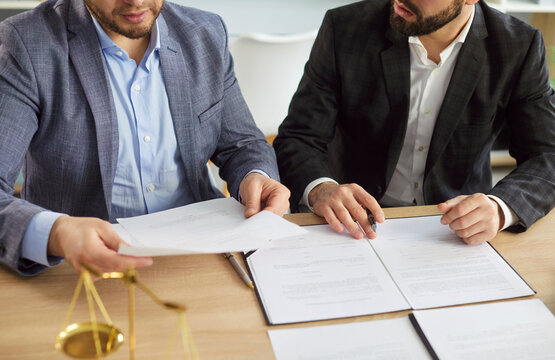 Close up, legal consultation between male client and professional lawyer in office. Reviewing documents and contract before signing, scales of justice on table, as symbol of fairness, legal process
