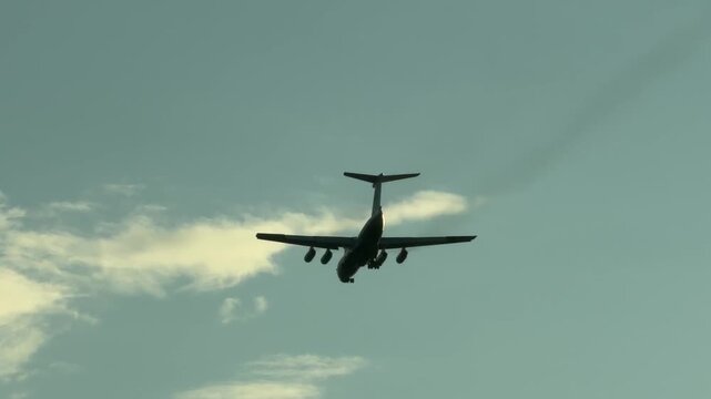 Large cargo airplane flying low, leaving a faint gray mist trail behind its jet engines during a landing approach. Aviation industry, transport concept, scenic rear view tracking video footage.