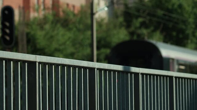 Metal fence creating a symbolic barrier, blurring background showing a passenger train passing by, suggesting movement and separation