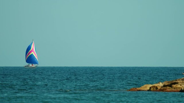 Sailboat smoothly navigating peaceful blue ocean under a clear sky, enjoying freedom and adventure with a colorful spinnaker