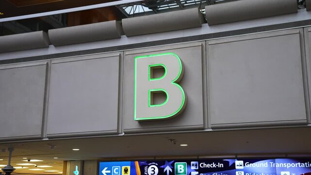 Close-up of the illuminated green "B" gate sign at Orlando International Airport, guiding travelers toward check-in, cruise transport, rental cars, and parking.