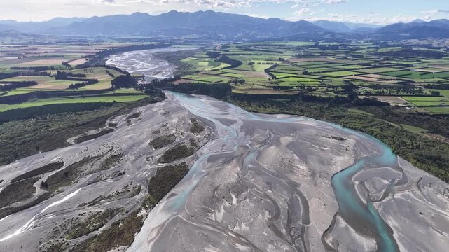 Drone aerial view of a braided river winding across the South Island of New Zealand, revealing intricate channels, gravel beds, and expansive rural landscapes.