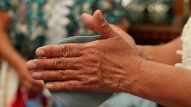 Hands shaping soft gray clay by hand during traditional pottery craft demonstration indoors, tossing and back and forth