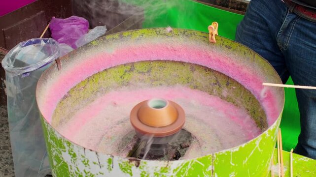 Cotton candy machine spinning sugar at vibrant carnival concession stand, medium overview