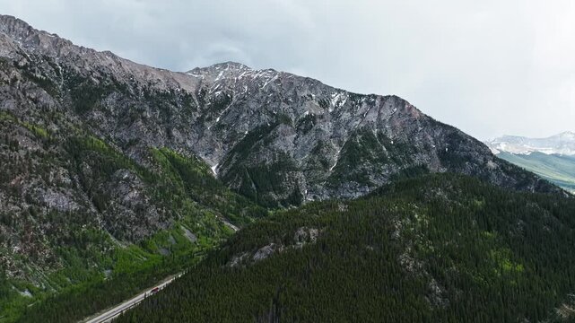 Rugged mountains above Frisco Gulch interstate and evergreen forest, drone pullback reveals straight path highway