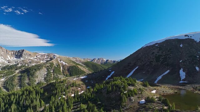 Alpine ridges with snow patches and evergreen forest at Loveland Pass, drone tilt up to beautiful sky, space for text in backdrop