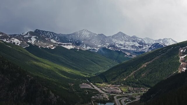 Sunlit alpine valley beneath rugged snow covered mountain peaks, drone overview of Wheeler Junction Colorado