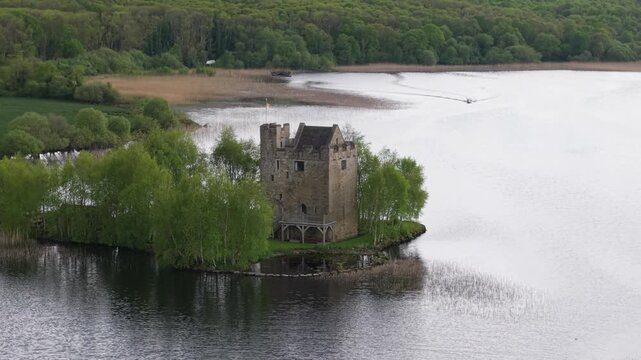 Ancient stone tower stands on small wooded island in calm lake, surrounded by forest