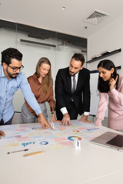 Diverse group of analysts professionals analyzing business strategy in charts and diagrams spread on table in office. Corporate finances management, market and sales research, or project planning