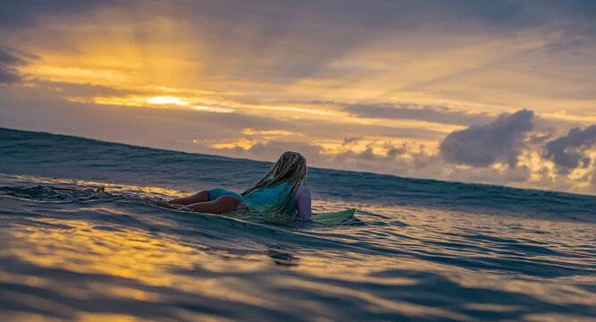 Surfer Girl Paddling Out to Watch Dramatic Sunset Sky Over Sea