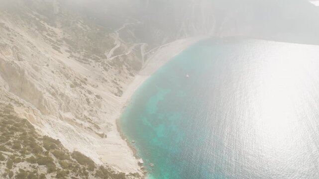 Foggy aerial view of dramatic beach and turquoise sea below cliffs in Cephalonia